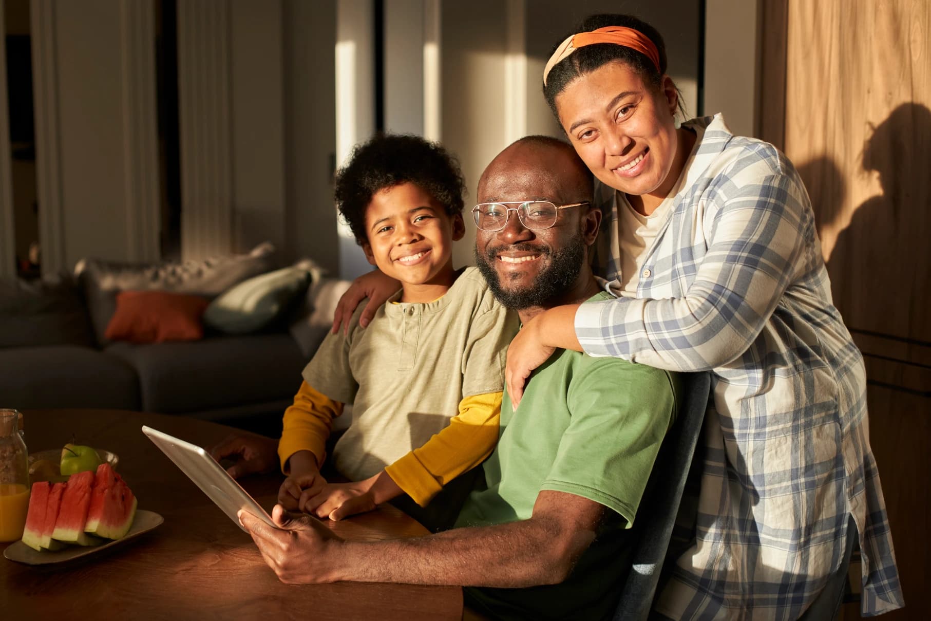 A man smiling with tablet on his hands, smiling with his family i.e., wife and kids